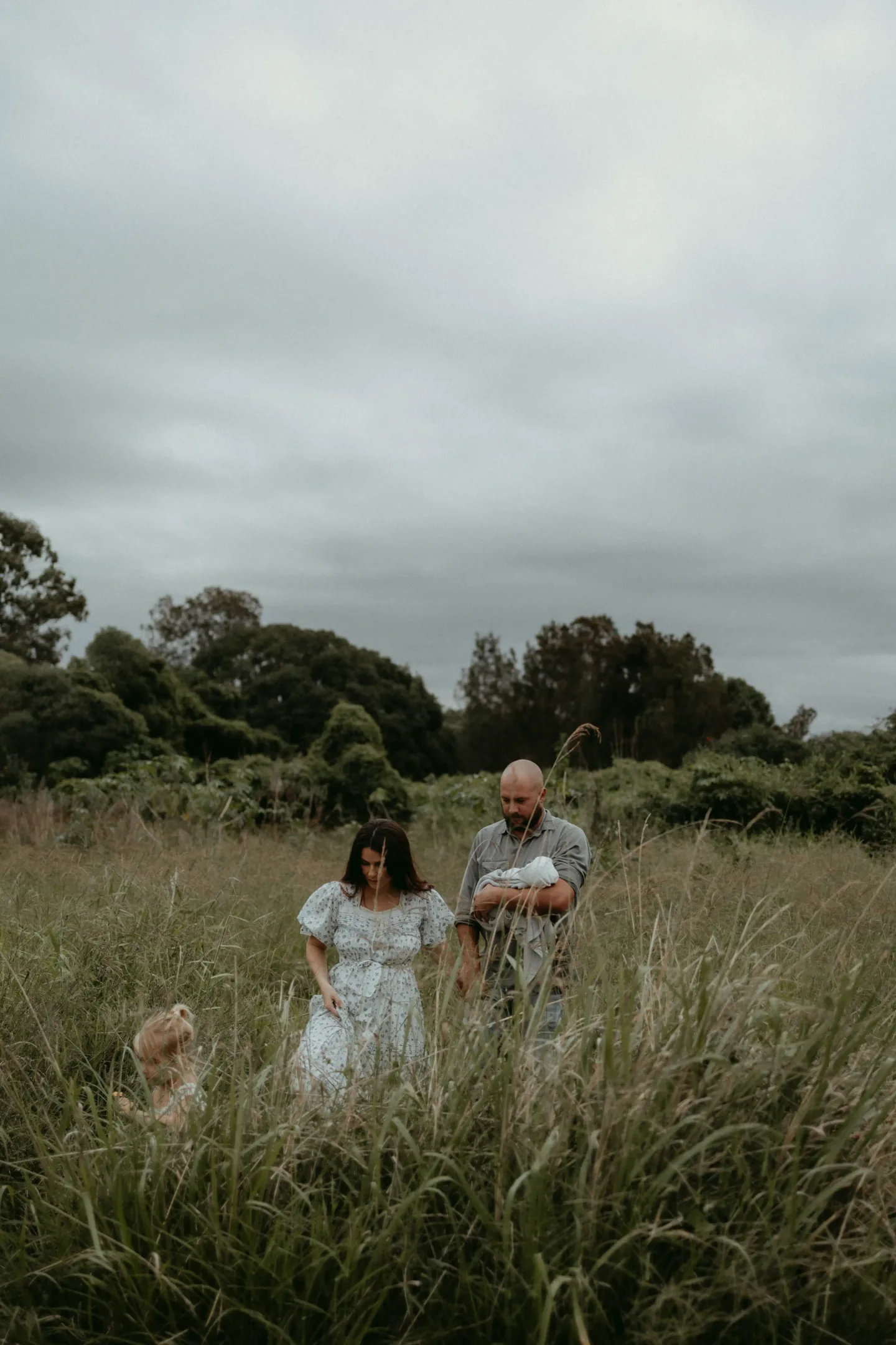 Family standing together in tall grass beneath a cloudy sky