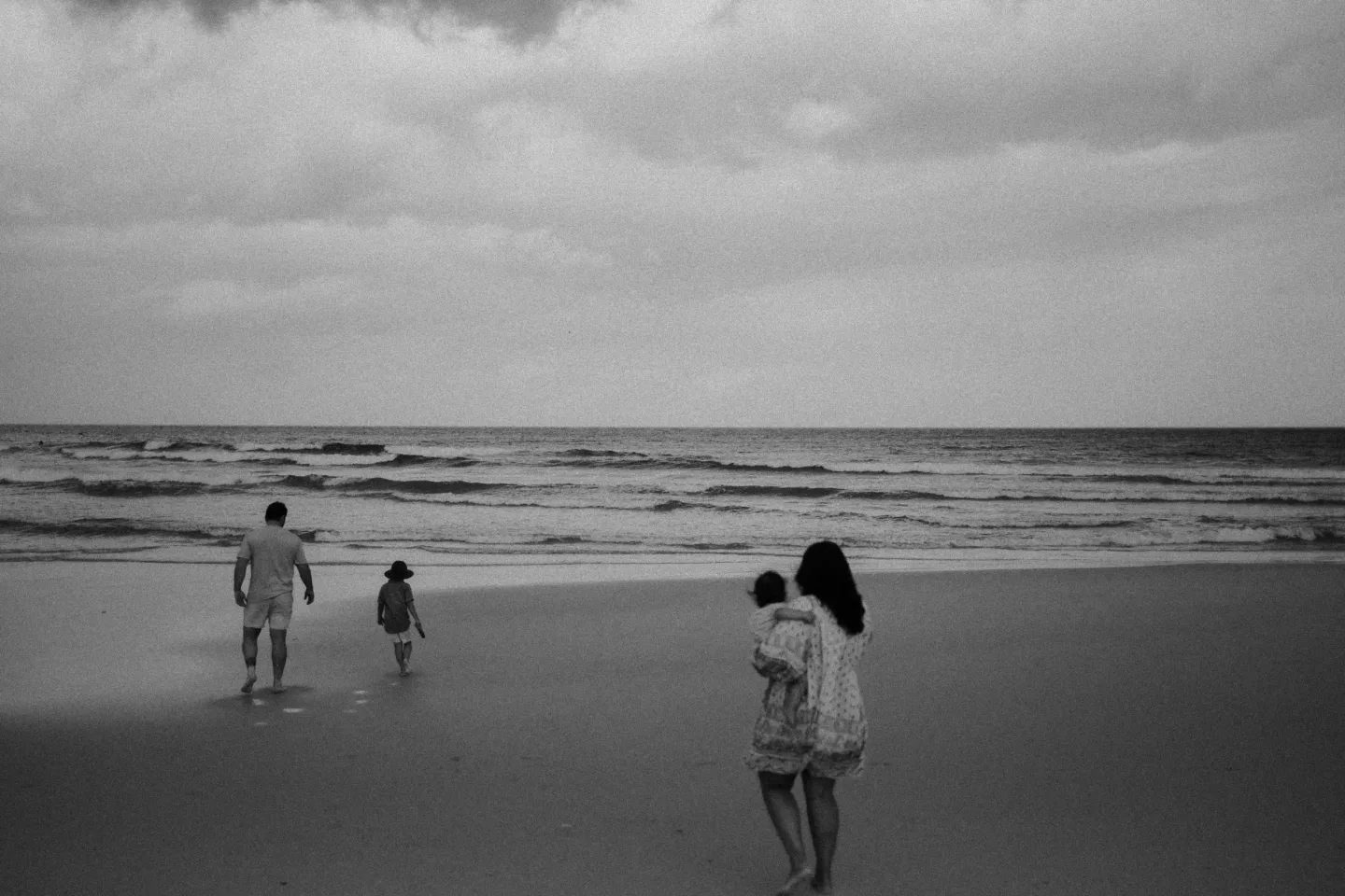 Black and white family photograph at the beach, with children walking towards the waves
